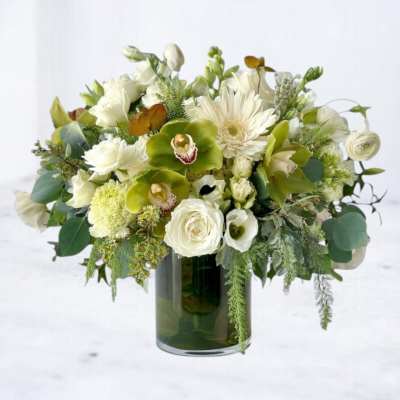 White and green mixed flower arrangement with orchids and roses in a clear glass cylinder vase