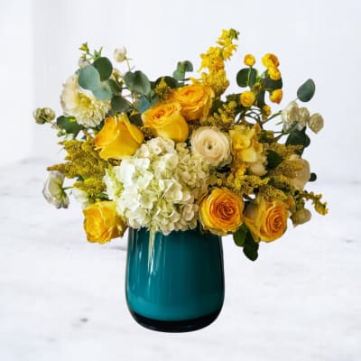 Yellow and white flower arrangement in a teal glass vase