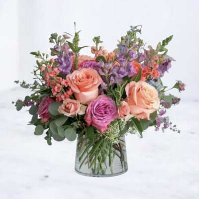 Mixed bouquet of peach and lavender roses with purple accents in a clear glass vase
