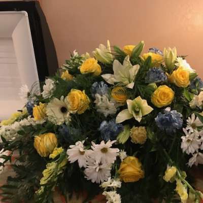 Large mixed floral arrangement with yellow roses, white lilies, and blue flowers