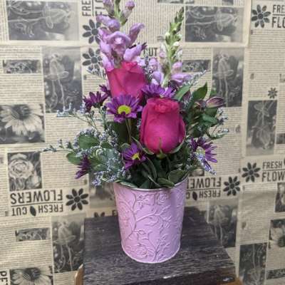 Pink roses and purple flowers arranged in a lavender metal pot