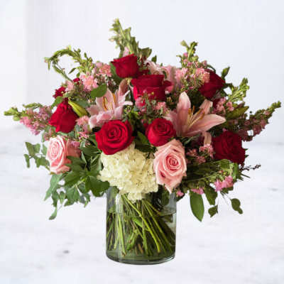 Arrangement of red and pink roses, pink lilies, and white hydrangea in a clear glass vase