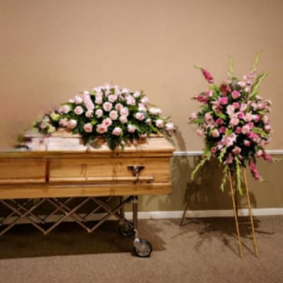 Casket with pink floral sprays on top and at both sides