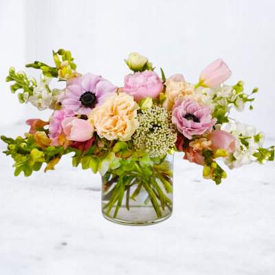 Low pastel arrangement of pink and peach flowers with anemones and tulips in a clear glass vase