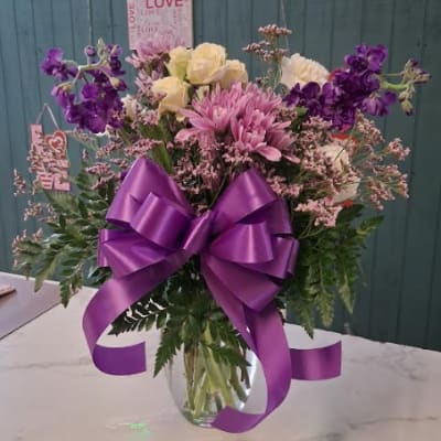Purple and pink mixed bouquet in a glass vase with a large purple ribbon