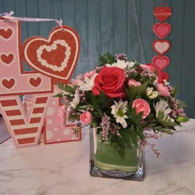 Pink and red floral arrangement in a glass vase with heart decorations