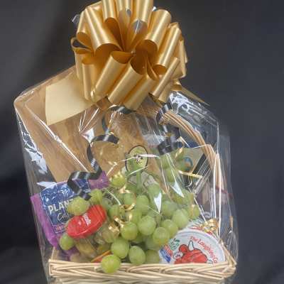 Gift basket with grapes, cheese, and crackers wrapped in cellophane with a gold bow
