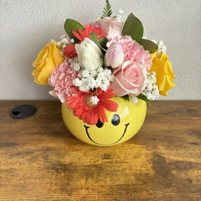 Pink and yellow flower arrangement in a smiley-face pot