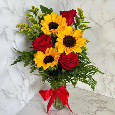 Bouquet of red roses and yellow sunflowers in a glass vase with a red ribbon