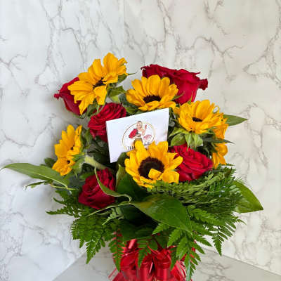 Bouquet of red roses and yellow sunflowers in a glass vase with a red ribbon