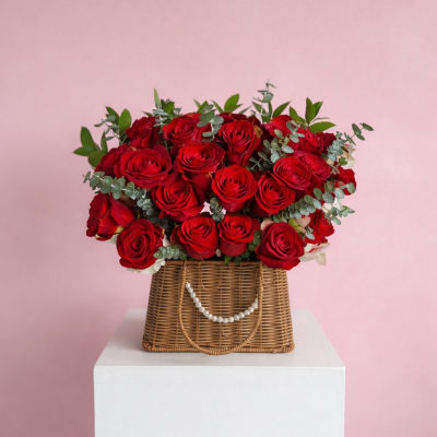 Red rose arrangement in a wicker basket with greenery