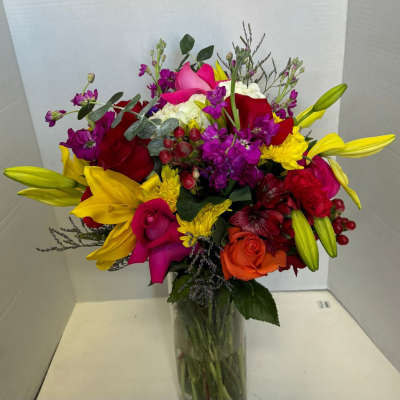Colorful bouquet with lilies, roses, calla lilies, and purple filler in a glass vase
