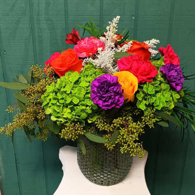 Colorful bouquet with roses, carnations, and hydrangeas in a textured vase