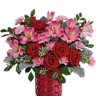 Red roses and pink flowers arranged in a red glass vase