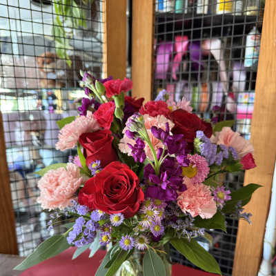 Mixed bouquet of red roses, pink carnations, and purple flowers in a glass vase