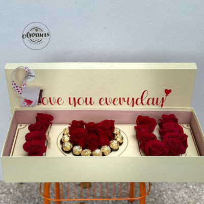 Cream gift box with red roses and gold-wrapped chocolates arranged around a heart of roses