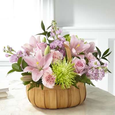 Pink lilies and roses arranged in a wooden basket with green accents