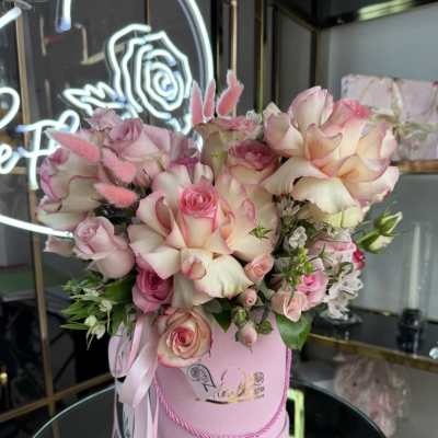 Pink and cream roses arranged in a round pink box with ribbon.