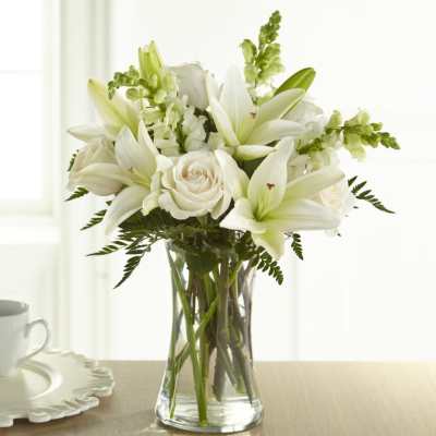 White lilies and roses arranged in a clear glass vase
