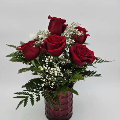 Red roses arranged in a purple glass vase with white filler flowers