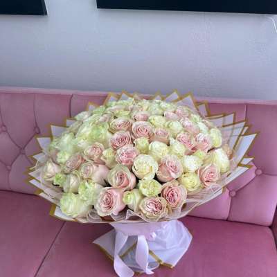 Large bouquet of pale pink and cream roses wrapped in white paper with gold trim