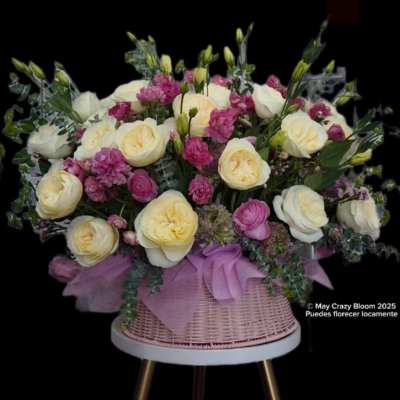 Pink and cream roses arranged in a wicker basket with a lavender ribbon.