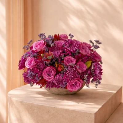 Low centerpiece of bright pink roses and chrysanthemums in a round bowl vase.