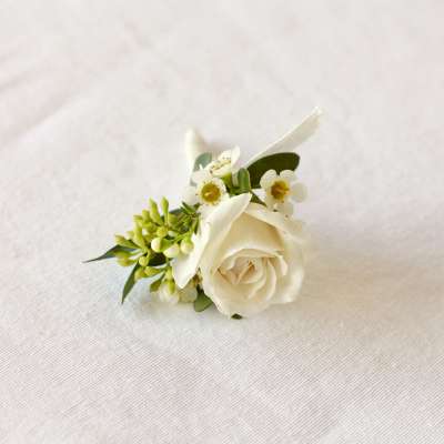 White rose boutonniere with small white blossoms and greenery