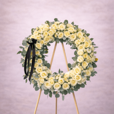 Large round wreath of pale yellow roses on a wooden easel with a black ribbon.