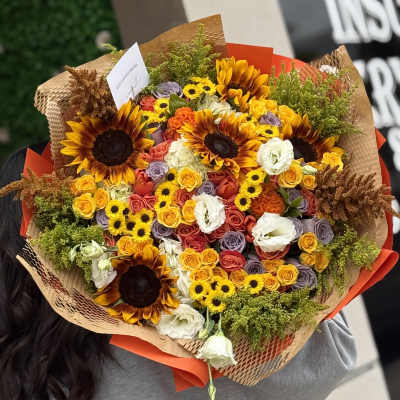 Large bouquet of sunflowers, roses, and white blooms wrapped in brown paper