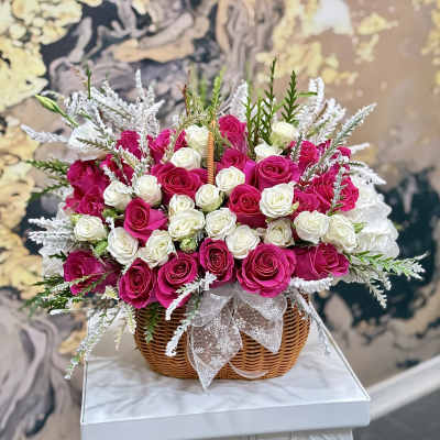 Basket of pink and white roses with frosted greenery and a ribbon bow
