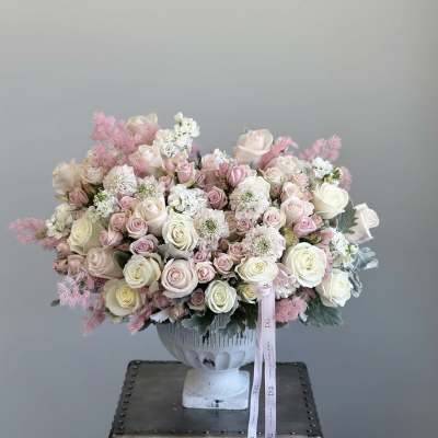 Large pastel bouquet of roses and white filler flowers in a white urn vase