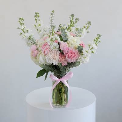 Pink and white bouquet in a clear glass vase with a pink ribbon