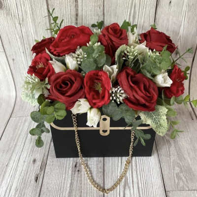 Red roses and white blooms arranged in a black box with a gold chain handle.