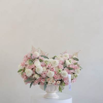 Pink and white rose arrangement in a white pedestal vase