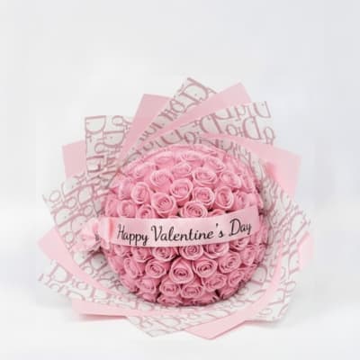 Round bouquet of pink roses wrapped in pink paper with a Valentine’s Day ribbon