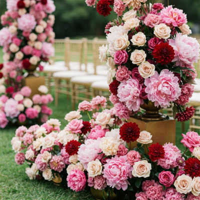 Pink and cream floral arrangements with red accents at an outdoor ceremony