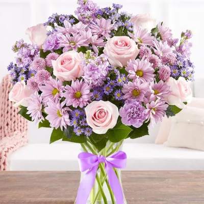 Pink and lavender bouquet of roses and daisies in a glass vase with a purple ribbon