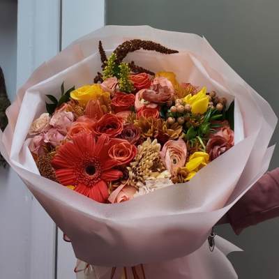 Bouquet of red, pink, and yellow flowers wrapped in pale pink paper