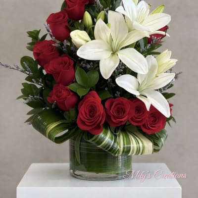 Arrangement of red roses and white lilies in a clear vase with decorative green leaves.