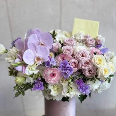 Lavender orchids and pink roses arranged in a pink vase