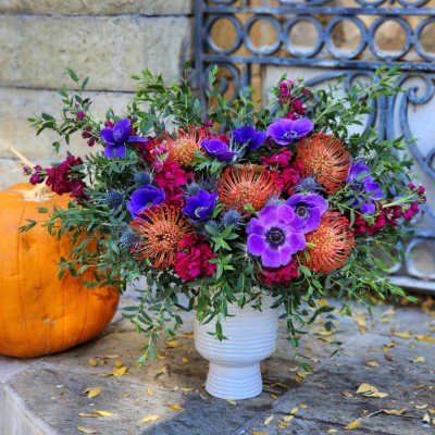 Purple and orange floral arrangement in a white vase beside a pumpkin