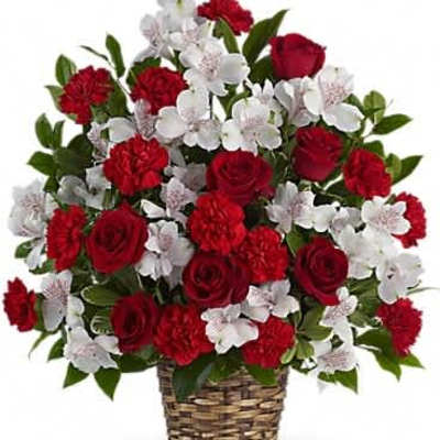 Red roses, red carnations, and white flowers arranged in a woven basket.