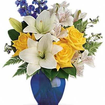 Arrangement of white lilies, yellow roses, and white alstroemeria in a blue glass vase