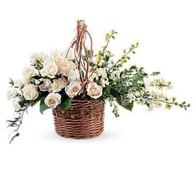 Ivory spray rose arrangement in a brown wicker basket with trailing blossoms.
