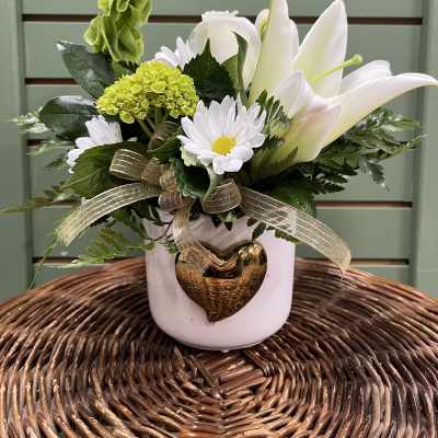 White lilies and daisies in a white vase with a gold heart ornament
