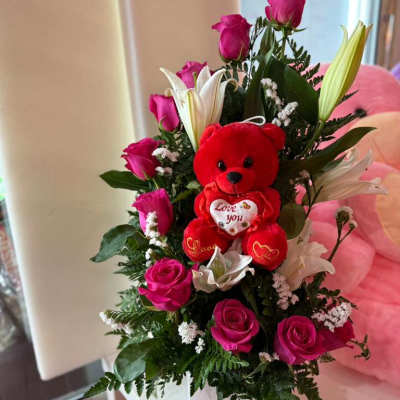 Pink roses and white lilies arranged with a red teddy bear in a white box