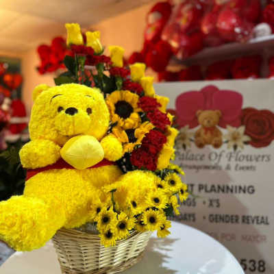 Yellow teddy bear in a wicker basket with red and yellow flowers