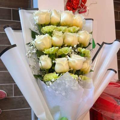Bouquet of white roses and pale green carnations wrapped in white paper