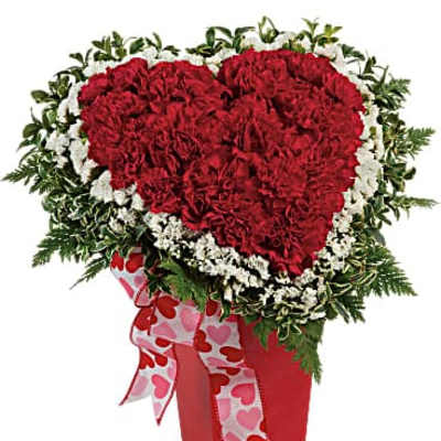 Heart-shaped red carnation arrangement in a red vase with a heart ribbon